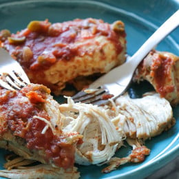 Partially shredded cooked salsa chicken on a blue plate next to two forks.