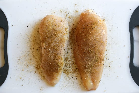 Two seasoned chicken breasts side by side on a cutting board.