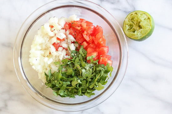 A mixing bowl with diced onion, diced tomato, chopped cilantro, and a half of a juiced lime