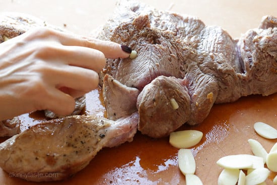A hand presses garlic slivers into small holes cut in the side of a browned pork shoulder.
