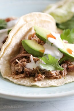 Instant Pot carnitas tacos on a plate topped with avocado slices, cilantro, and cheese.