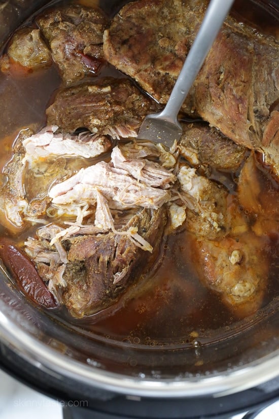 A fork stuck into cooked and partially shredded pork shoulder inside the Instant Pot.