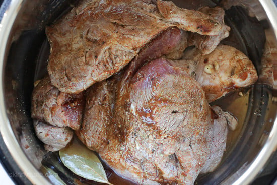 Browned pork shoulder inside the Instant Pot with broth and bay leaves.