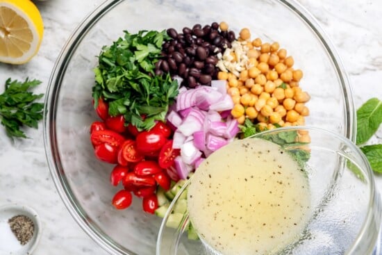 Pouring lemon dressing into bowl with bean salad ingredients.