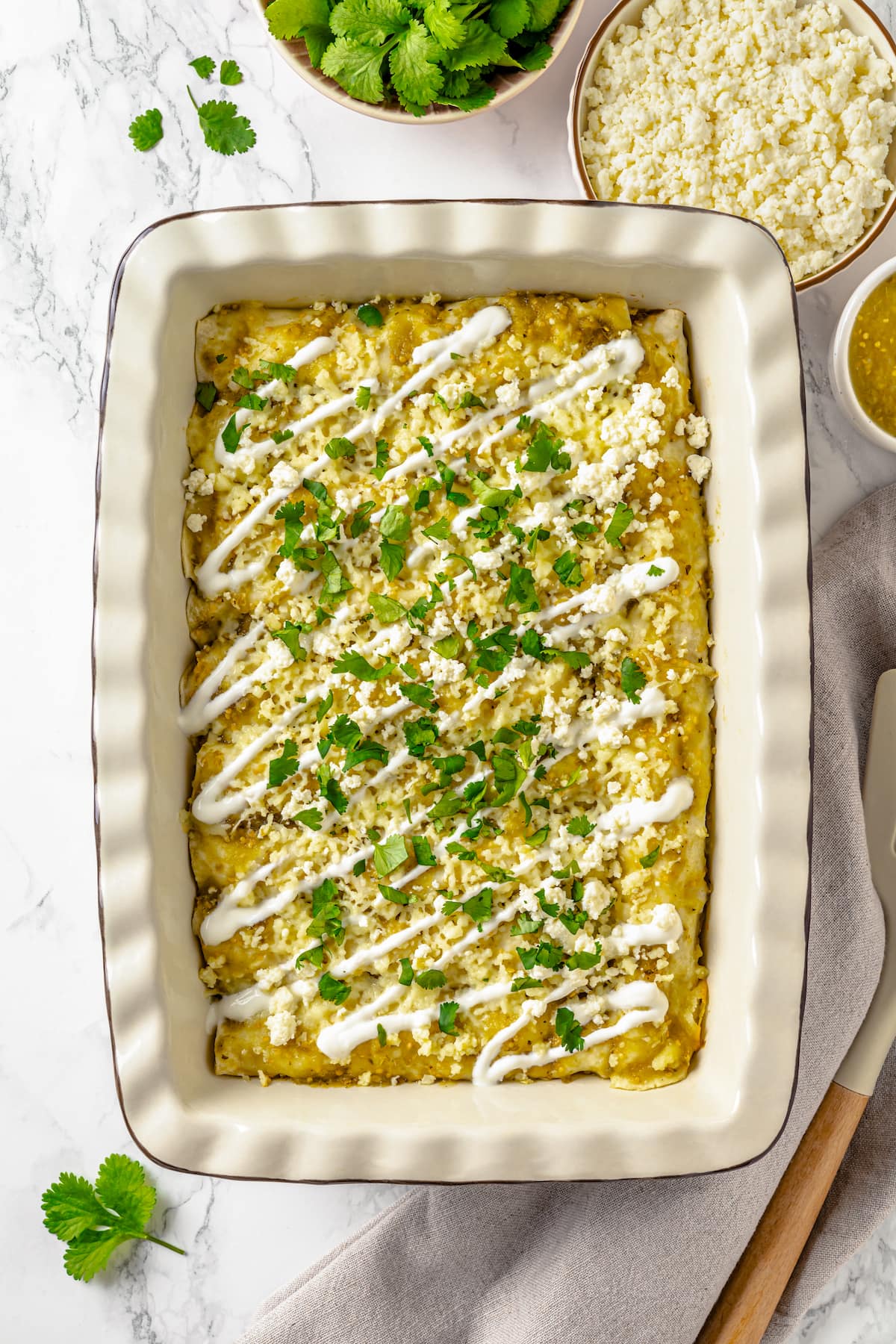 A casserole dish of enchilada verdes topped with sour cream and cilantro