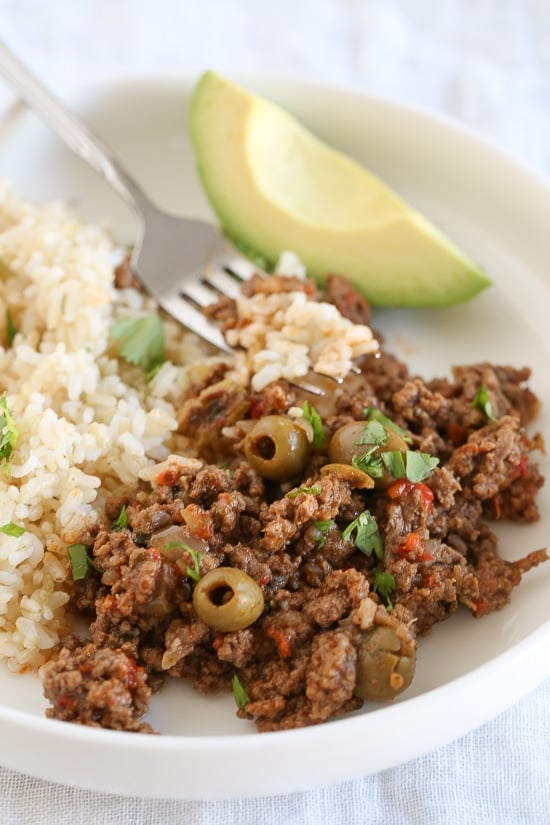 A plate of picadillo with rice and an avocado slice