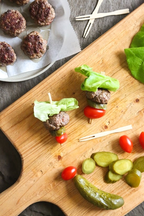 Mini burgers with bacon, layered on a bamboo skewer with lettuce, tomatoes and pickles! Who can resist your favorite foods on a stick – not me! These burger bites make the perfect low-carb appetizer to please everyone from age six to age sixty, just set out some ketchup and mustard for dipping and watch them disappear.