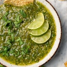 Bowl of salsa verde with 3 lime wedges and chip
