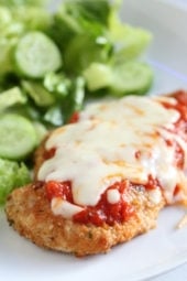 Chicken parmesan next to salad on a plate.