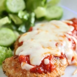 Chicken parmesan next to salad on a plate.