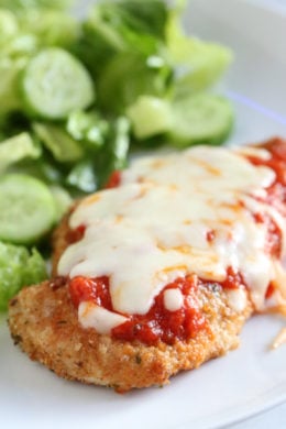 Chicken parmesan next to salad on a plate.