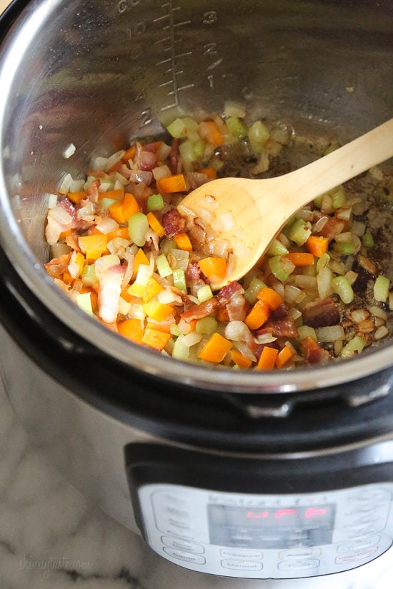Diced veggies sauteing inside the Instant Pot next to a wooden spoon.