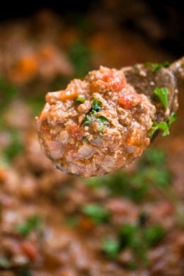 Close up of a spoonful of bolognese sauce held over a pot of sauce.