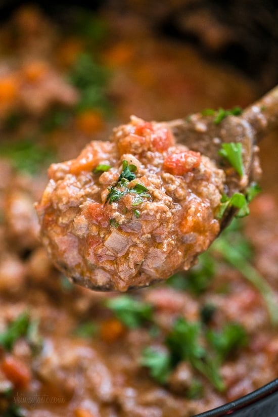 Close up of a spoonful of bolognese sauce held over a pot of sauce.