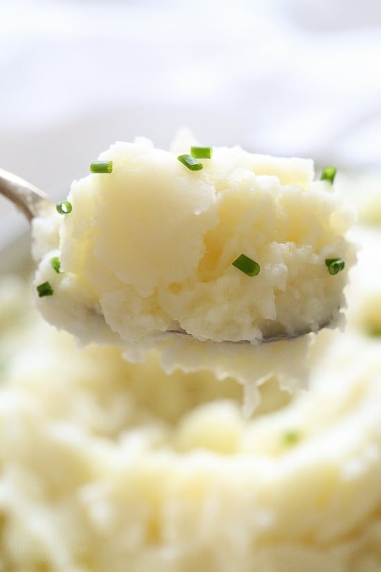 A spoonful of Instant Pot mashed potatoes sprinkled with chopped chives, with more mash in the background.