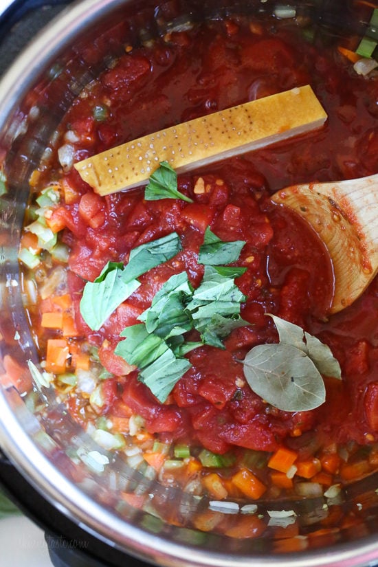 A wooden spoon stirring tomatoes into veggies in the Instant Pot
