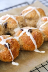 Close up of hot cross buns topped with icing on a parchment-lined rack.