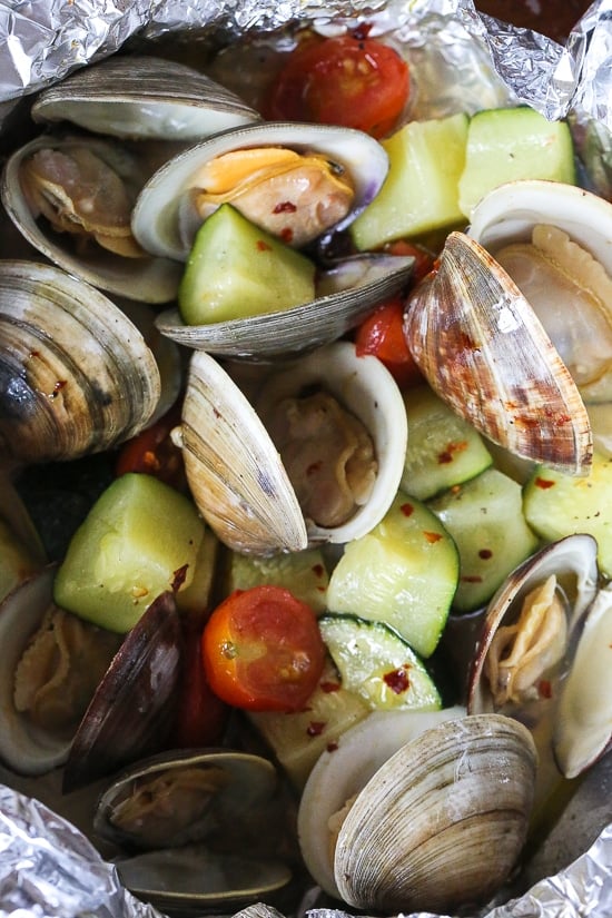 Grilled little neck clams cooked in foil packets with zucchini and tomatoes in a garlic white wine sauce, so fast and easy, perfect to make all summer long!