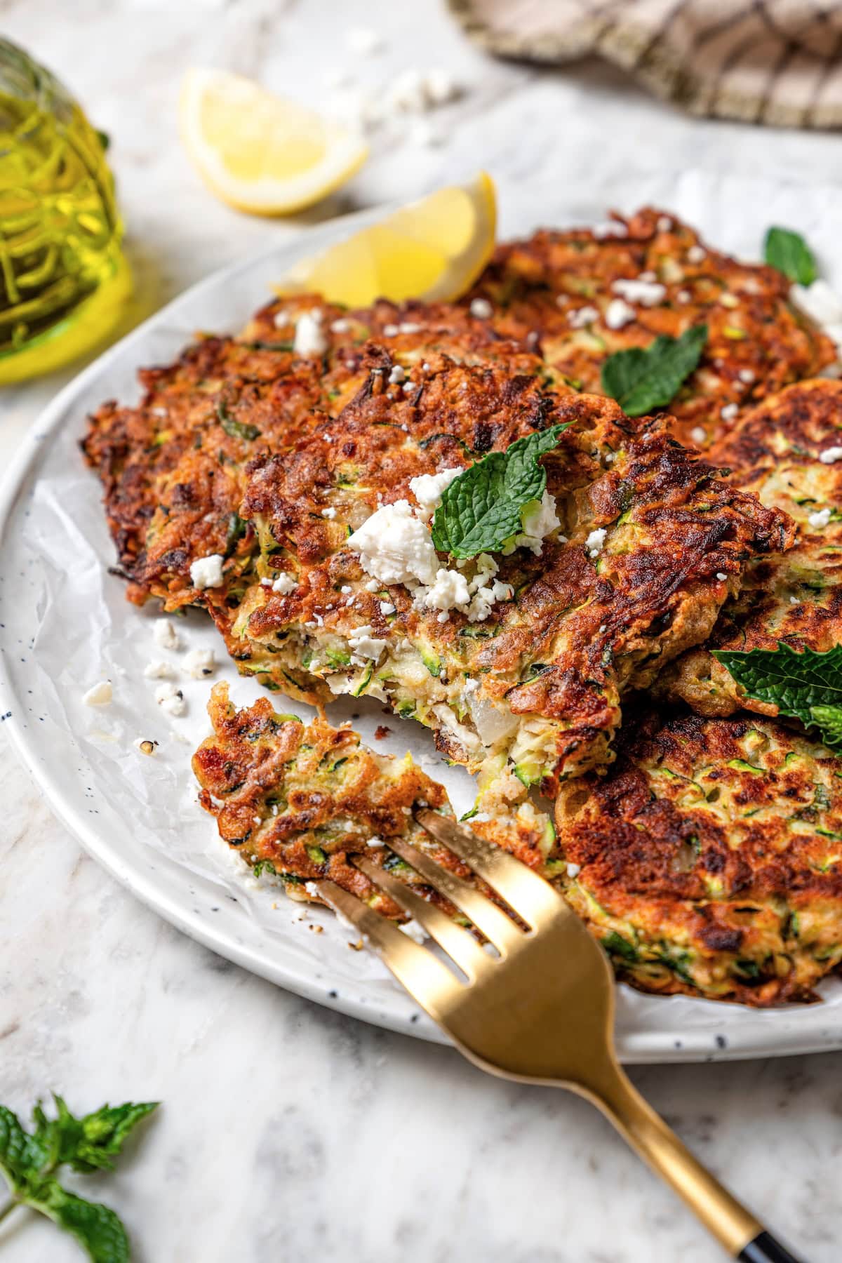 These easy zucchini fritters are crunchy, cheesy, and full of Mediterranean flavor! Serve as a summer side dish, appetizer, or light meal. Zucchini fritters on plate with fork.