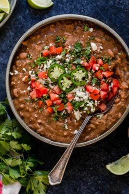A bowl of refried beans topped with diced tomatoes and jalapeno
