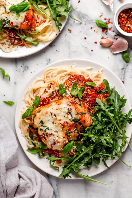 Overhead view of two plates of Instant Pot chicken parm with spaghetti noodles and greens