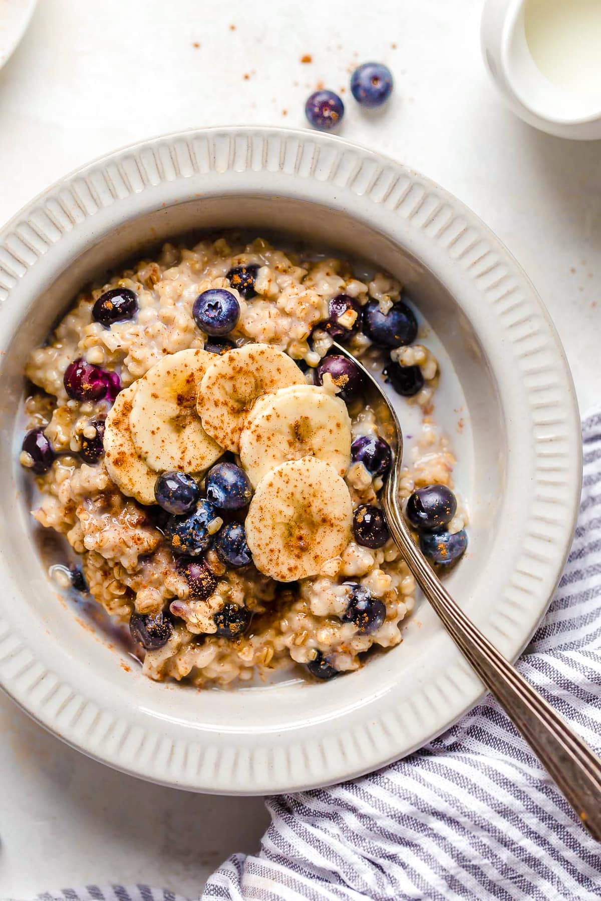 A spoon in a bowl of oats with blueberries and bananas.