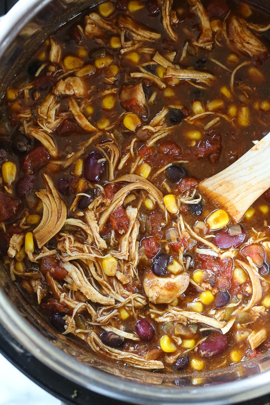 Chicken taco chili in the Instant Pot being stirred by a wooden spoon