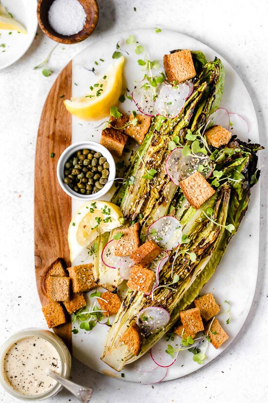 Grilled romaine makes this salad a standout! You’ll love the creamy vegan Caesar dressing, which is made with raw cashews instead of egg. Grilled romaine salad on marble and wood cutting board.