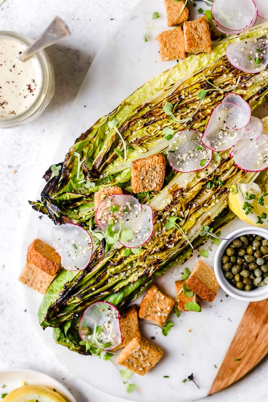 Grilled romaine makes this salad a standout! You’ll love the creamy vegan Caesar dressing, which is made with raw cashews instead of egg. Grilled romaine salad with vegan Caesar dressing on marble and wood board.