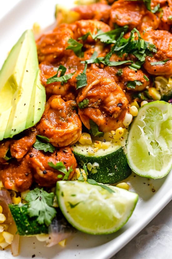 This delicious Mexican Shrimp dish is made with saucy Chipotle shrimp served over a bed of corn, zucchini, and red onions, and served with a side of avocado.