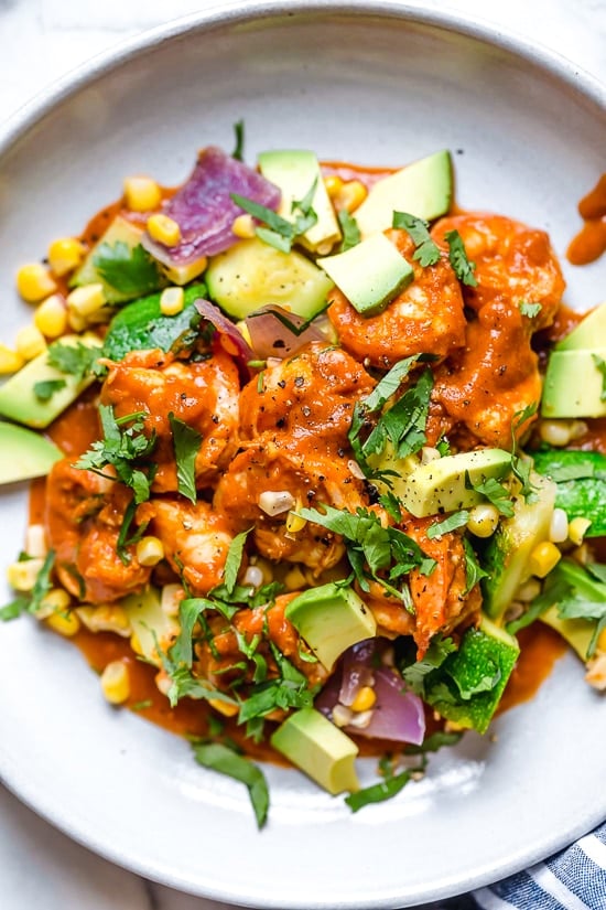 This delicious Mexican Shrimp dish is made with saucy Chipotle shrimp served over a bed of corn, zucchini, and red onions, and served with a side of avocado.