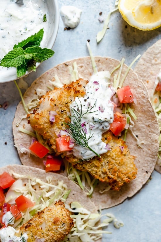 Tzatziki Fish Tacos have a Greek twist! Crisp breaded fish fillets served on tortillas topped with tzatziki sauce made with Greek yogurt, cucumbers and fresh herbs.