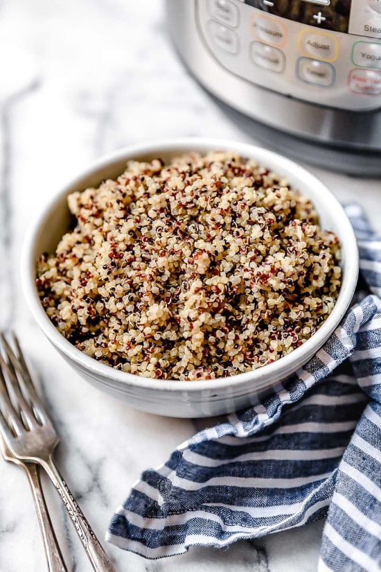 A bowl of cooked quinoa on a marble counter next to an Instant Pot.