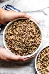 Overhead view of two hands wrapped around a white bowl of perfect, fluffy Instant Pot quinoa.