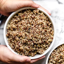 Overhead view of two hands wrapped around a white bowl of perfect, fluffy Instant Pot quinoa.