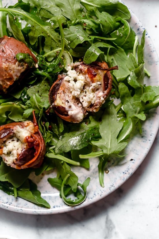 Prosciutto Wrapped Figs with Blue Cheese served on a bed of baby arugula with a light vinaigrette. A delicious combination of salt, acid and sweet.