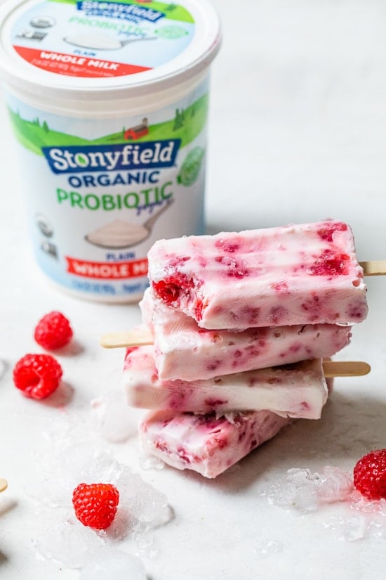 Raspberry Yogurt Ice Pops stacked with yogurt tub in background