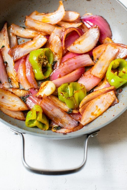sauteed red onion, green peppers in a skillet.
