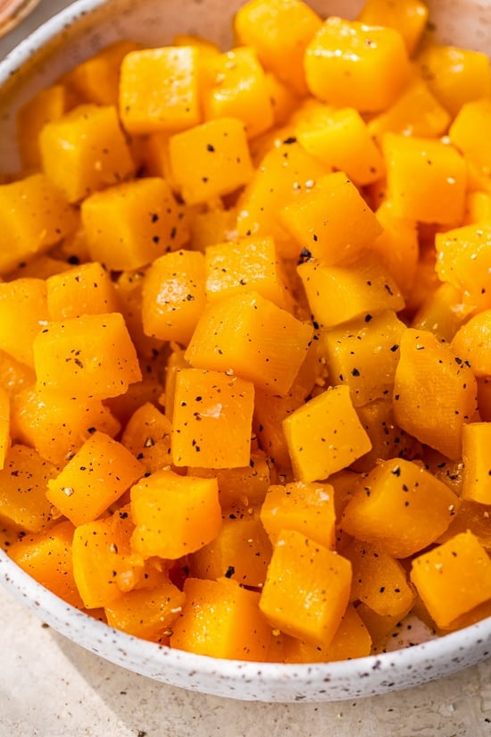This easy maple roasted butternut squash is a quick fall side dish with cubed squash tossed in pure maple syrup. Perfect for holiday dinners! Close up of maple roasted butternut squash in a large bowl.