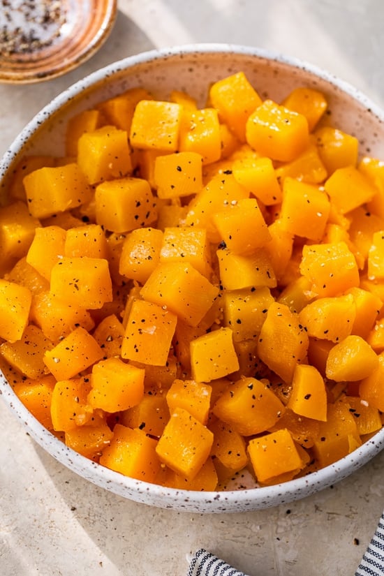 This easy maple roasted butternut squash is a quick fall side dish with cubed squash tossed in pure maple syrup. Perfect for holiday dinners! Diced maple roasted butternut squash with black pepper in a white bowl.