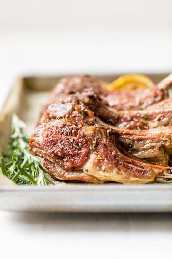 Frenched Rack of Lamb on a sheet pan with rosemary.