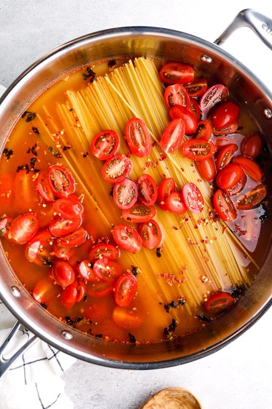 pasta, tomates y agua en una sartén antes de cocinar