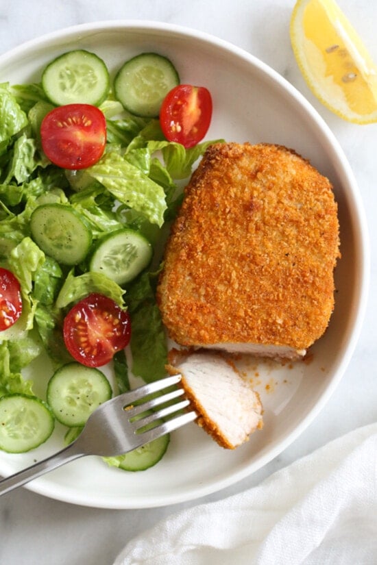 Breaded air fryer pork chops with lettuce, tomatoes, cucumbers, and a fork