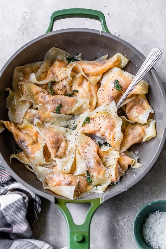 This easy butternut squash ravioli is made with wonton wrappers and tossed with sage butter for a delicious, restaurant-style pasta dinner. Butternut squash ravioli with sage butter and grated cheese in a skillet.