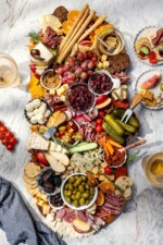 Plates surrounding large charcuterie and cheese board with fruit, pickles, olives, and spreads.