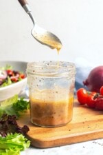 Greek salad dressing drizzling from spoon into jar.