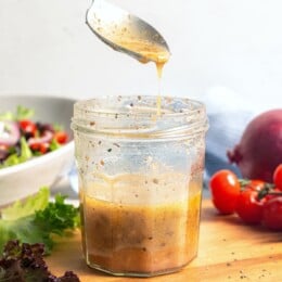 Greek salad dressing drizzling from spoon into jar.