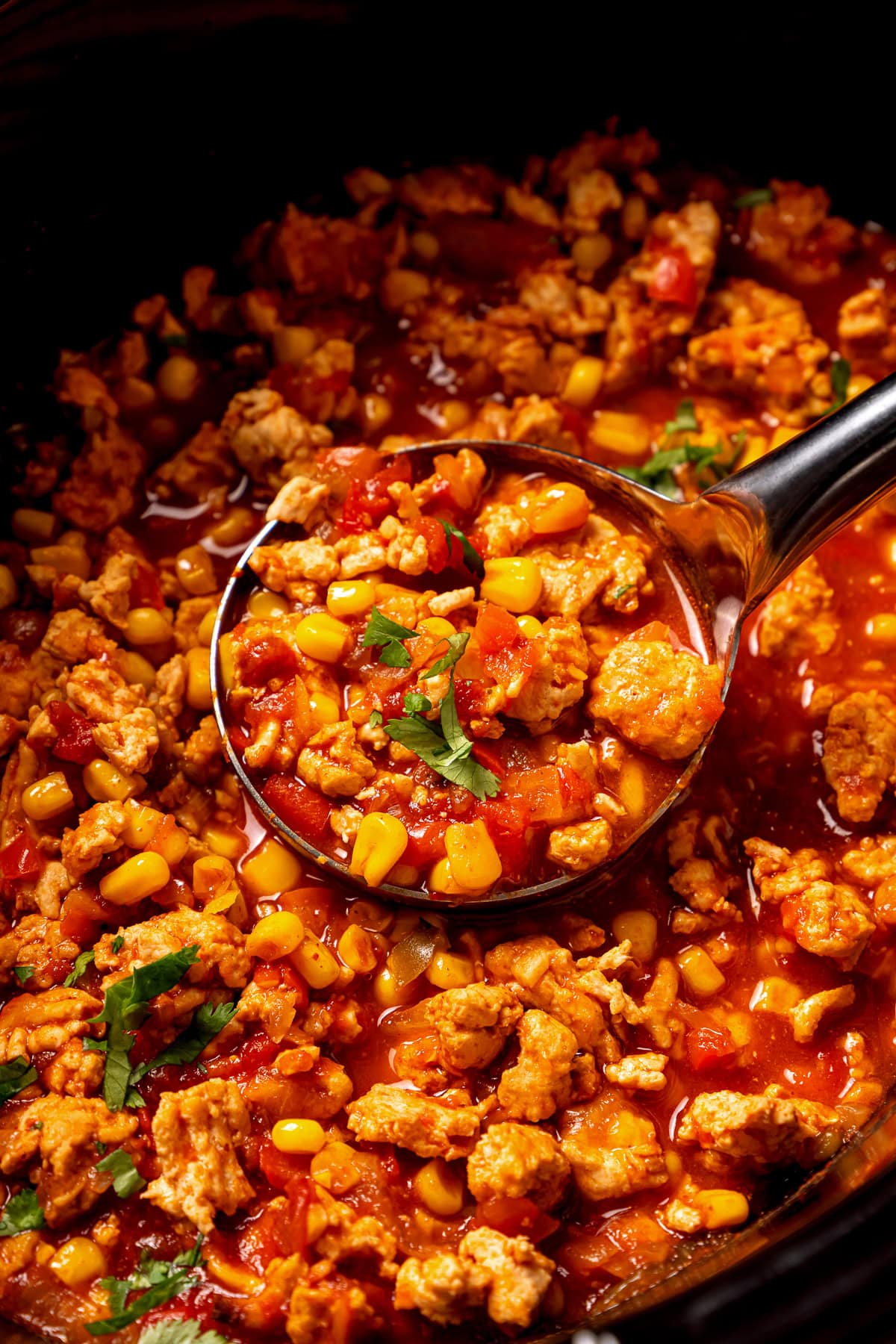 This crock pot turkey chili recipe is easy to make and family-friendly, with ground turkey, corn, bell pepper, tomatoes, and mild spices. Close up of a ladle scooping turkey chili inside the crock pot.