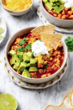 A bowl of turkey chili garnished with sour cream, diced avocado, tortilla chips, and cilantro.