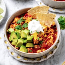 A bowl of turkey chili garnished with sour cream, diced avocado, tortilla chips, and cilantro.